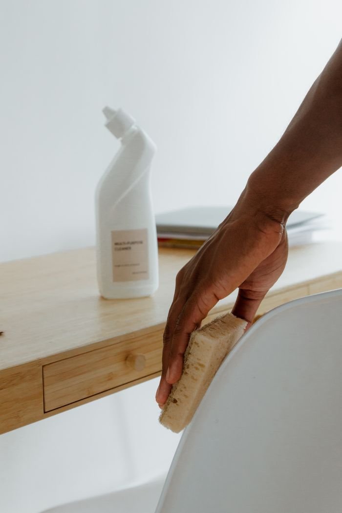 About Minimalist room with a person cleaning a chair using a sponge and cleaning product.