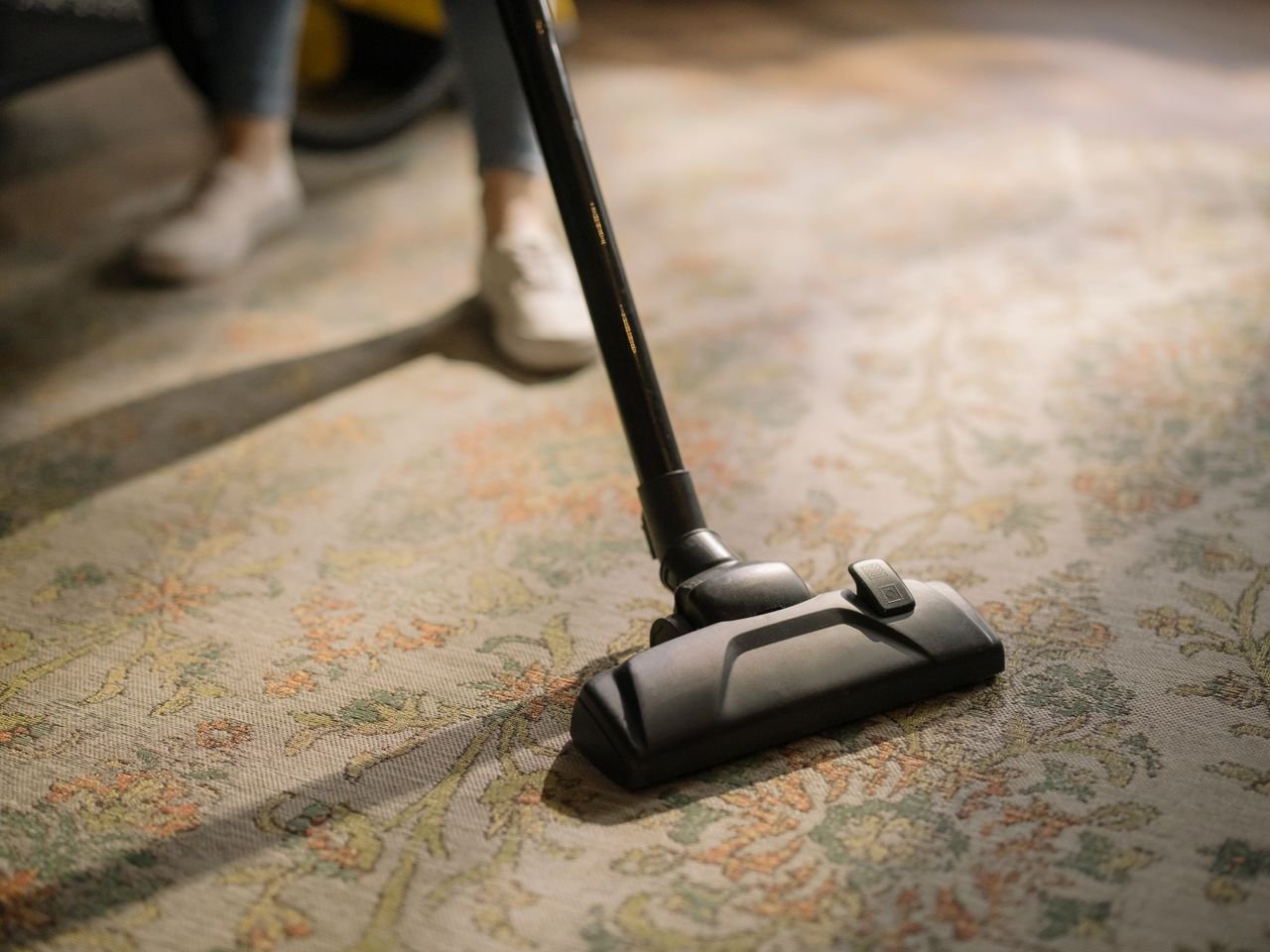 Home Close-up of a vacuum cleaner on a patterned carpet in a sunlit room, capturing a moment of household cleaning.