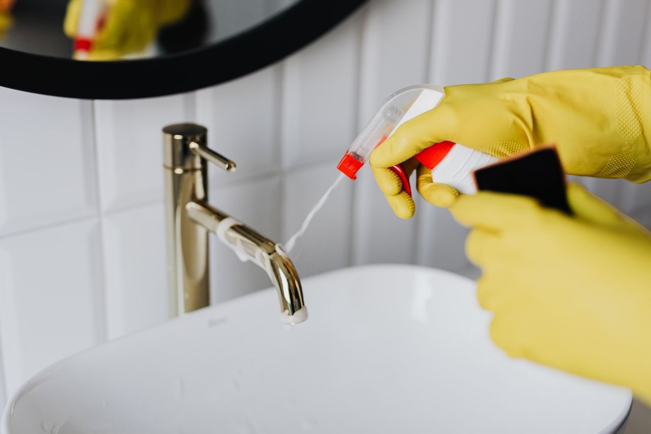 Home From above anonymous housekeeper in yellow rubber gloves spraying cleaner to chrome water faucet in bathroom